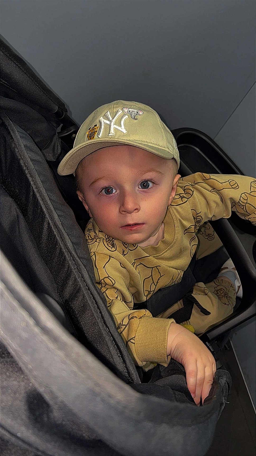 Kayden participe au concours pour gagner de l'argent avec cette photo : toddler, child, stroller, cap, beige_clothing, blue_eyes, face, hand, curious, person, infant, patterned_outfit, seated, indoor, portrait, young_child, baby, casual_wear, headwear, looking_up