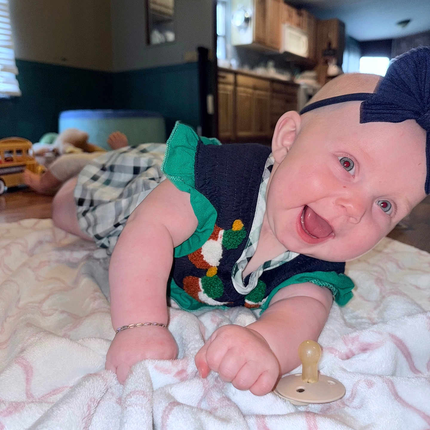 Laiken joined the competition — help win amazing prizes! baby, blanket, bracelet, cabinet, child, closeup, dress, floor, happy, headband, home, indoors, infant, kitchen, lying_down, pacifier, person, smiling, toy, wooden_floor