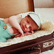 Lohan a rejoint le concours — aidez-le/la à gagner de superbes lots ! baby, newborn, sleeping, hat, green_outfit, knitted_blanket, vintage_suitcase, soft_texture, cozy, peaceful, infant, cute, portrait, resting, indoor, child, person, warm, sleep, relax