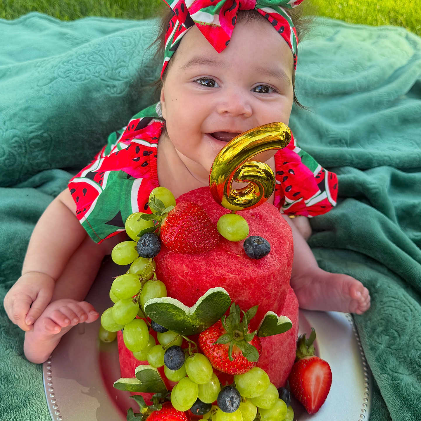Nyla is registered to the contest to win money with this photo: baby, child, fruit_cake, watermelon, grapes, strawberries, blueberries, green_blanket, outdoor, headband, smile, happy, celebration, number_6, plate, cute, summer, grass, portrait, colorful