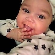 Nyla is registered to the contest to win money with this photo: baby, infant, child, face, hand, clothing, headwear, smile, cute, portrait, black_background, patterned_clothes, fingers, playful, young, closeup, expression, person, baby_girl, adorable