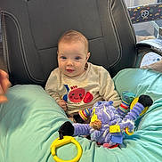 Amélia a rejoint le concours — aidez-le/la à gagner de superbes lots ! baby, child, toy, plush_toy, pillow, chair, sweater, indoor, playpen, colorful, smiling, seated, person, face, cute, comfort, bright_eyes, soft_lighting, playful, infant