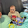 baby, child, toy, plush_toy, pillow, chair, sweater, indoor, playpen, colorful, smiling, seated, person, face, cute, comfort, bright_eyes, soft_lighting, playful, infant
