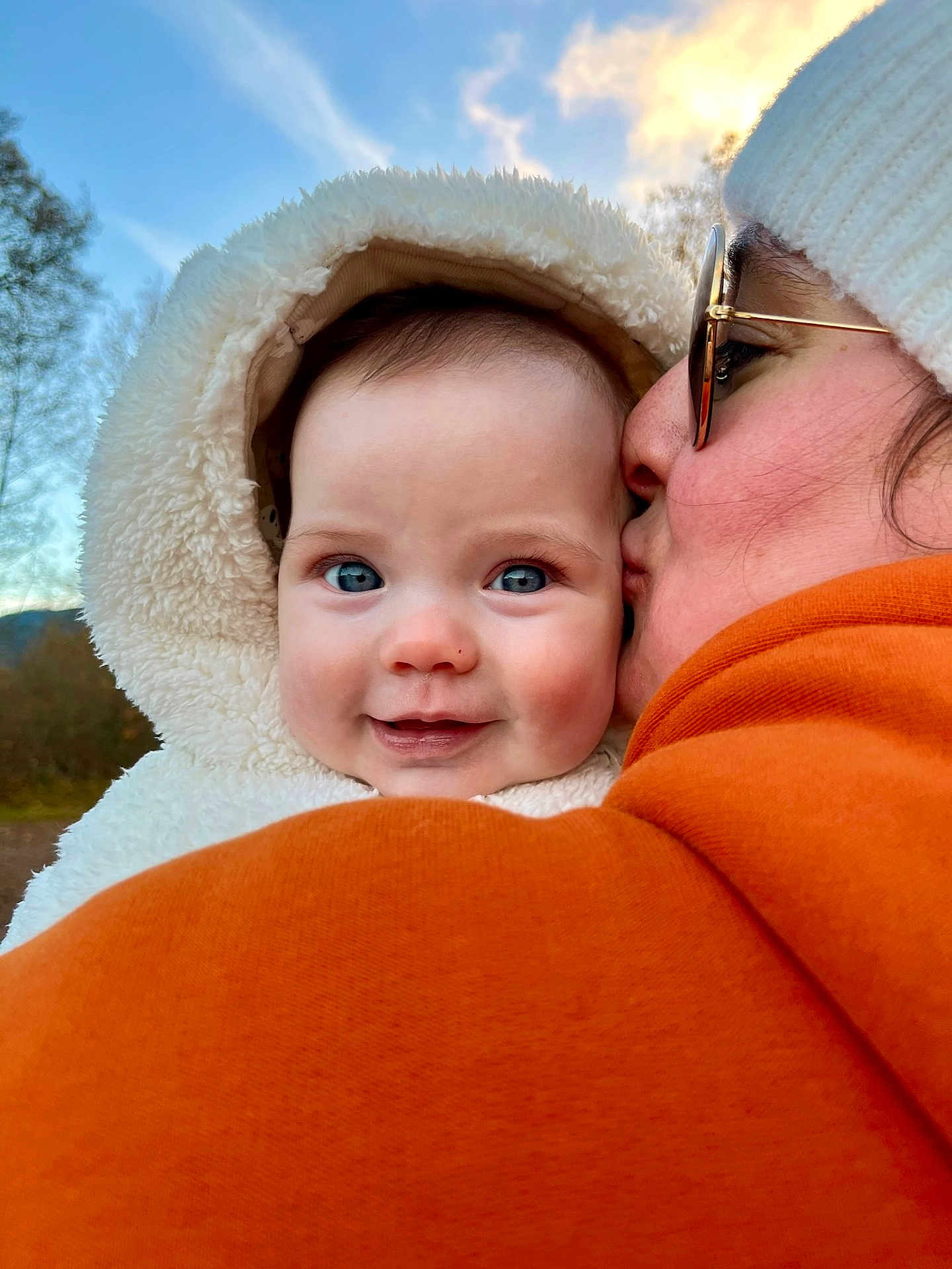 Amélia a rejoint le concours — aidez-le/la à gagner de superbes lots ! baby, child, person, face, blue_eyes, hood, jacket, knit_hat, kiss, outdoor, sky, clouds, trees, smile, warm_clothing, close_up, winter, affection, portrait, nature