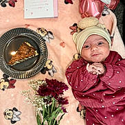 Minha is registered to the contest to win money with this photo: baby, infant, blanket, mickey_mouse, polka_dot, clothing, cake, candle, flowers, bouquet, card, plate, pink, maroon, smiling, cute, lying_down, indoors, celebration, headwear