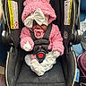 Oriah is registered to the contest to win money with this photo: baby, infant, car_seat, pink_clothing, pacifier, bow, sleeping, child, cute, fluffy, gloves, footwear, black_car_seat, indoors, safety_harness, newborn, headwear, toddler, resting, adorable