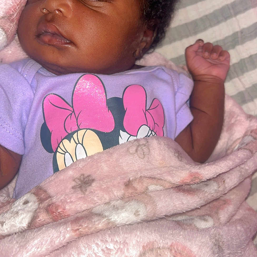Oriah joined the competition — help win amazing prizes! baby, sleeping, blanket, onesie, purple_clothing, minnie_mouse, infant, child, cute, peaceful, cozy, curly_hair, soft_texture, face, hand, resting, portrait, indoor, pink, toddler