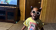 Kamorah joined the competition — help win amazing prizes! child, toddler, sunglasses, toy, indoor, carpet, wood_paneling, television, shoe, crocs, pink_pants, yellow_shirt, person, home, door, cabinet, living_room, playful, fun, portrait