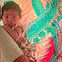 Nyla joined the competition — help win amazing prizes! baby, infant, child, person, adult_arm, colorful_background, abstract_art, pattern, curly_hair, clothing, holding, portrait, skin, face, bright_colors, red, teal, hand, foot, expression