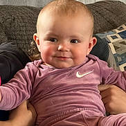 Renesmee is registered to the contest to win money with this photo: baby, child, infant, pink_clothing, nike_logo, smile, face, couch, pillow, person, indoors, hands, sitting, cute, soft_texture, happy, portrait, young_child, cozy, casual