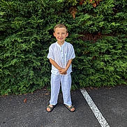 Tiago participe au concours pour gagner de l'argent avec cette photo : child, boy, smile, white_clothing, short_hair, greenery, bush, outdoor, parking_lot, asphalt, footwear, sandals, standing, happy, nature, casual, summer, portrait, person, daylight