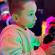 Evan a rejoint le concours — aidez-le/la à gagner de superbes lots ! child, hoodie, arcade, controller, colorful_lighting, neon, gaming, profile, young_boy, indoor, focused, portrait, casual_clothing, entertainment, technology, hands, short_hair, vibrant_colors, amusement, playful