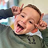 Evan participe au concours pour gagner de l'argent avec cette photo : child, boy, tongue_out, playful, green_sweatshirt, hands, face, expression, indoor, casual_clothing, short_hair, smiling, cute, portrait, person, young, fun, gesture, happy, closeup