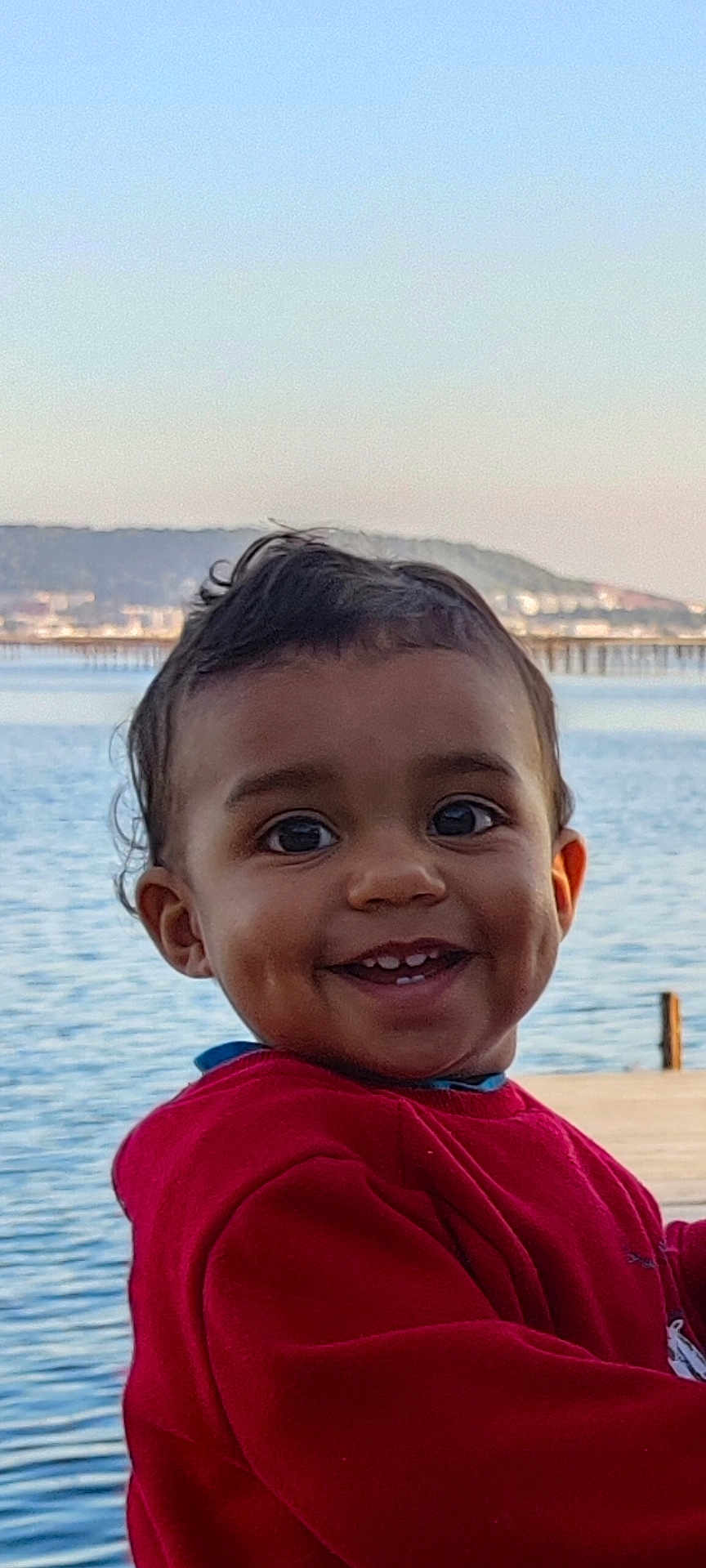Elyot participe au concours pour gagner de l'argent avec cette photo : toddler, child, smiling, face, red_sweater, outdoor, lake, water, hills, sky, portrait, happy, dimples, person, young_child, cute, nature, daylight, clothing, closeup
