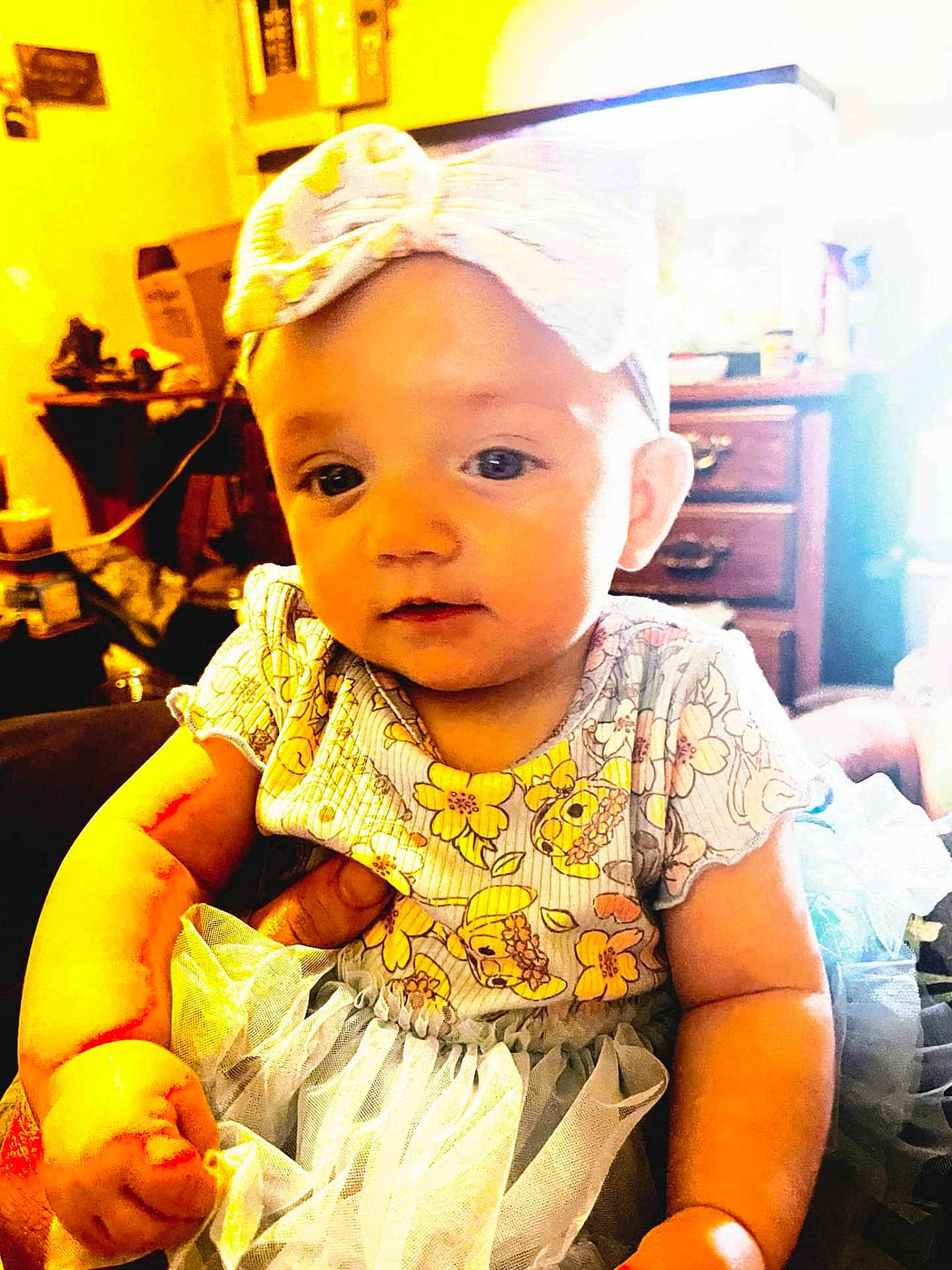 Oakley is registered to the contest to win money with this photo: baby, child, headband, bow, tutu, dress, floral_pattern, indoor, furniture, drawer, hand, person, cute, infant, smiling, portrait, holding, soft_lighting, tulle, young_child
