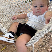Zavian is registered to the contest to win money with this photo: baby, child, toddler, portrait, face, eyes, serious_expression, outdoor, hammock, rope, sitting, lying_down, white_shirt, black_shorts, sneakers, socks, playground, dirt, gravel, photography