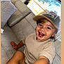 Elie participe au concours pour gagner de l'argent avec cette photo : toddler, child, smiling, cap, beige_clothing, couch, indoor, happy, portrait, hand, window, natural_light, sitting, face, person, casual, home, young_child, cute, joyful