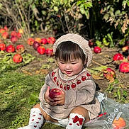 Tiana is registered to the contest to win money with this photo: toddler, child, apple, knitted_hat, knitted_sweater, grass, autumn, outdoor, fruit, red_apple, bag, socks, cute, smiling, nature, leaf, sunlight, garden, happy, sitting