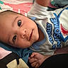 Javian is registered to the contest to win money with this photo: baby, infant, child, portrait, lying_down, indoors, blanket, bedding, clothing, shark_graphic, blue, pink, green, brown_hair, face, eyes, smiling, hand, cozy, close_up
