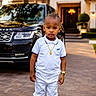toddler, child, white_clothing, sneakers, gold_watch, gold_chain, luxury_car, range_rover, driveway, house, outdoor, fashion, portrait, serious_expression, urban, pavement, sunset_light, person, standing, casual