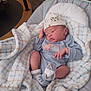 baby, newborn, blanket, baby_seat, hat, onesie, socks, plaid, indoor, floor, wood_floor, infant, clothing, cute, sleepy, resting, child, person, soft, cozy