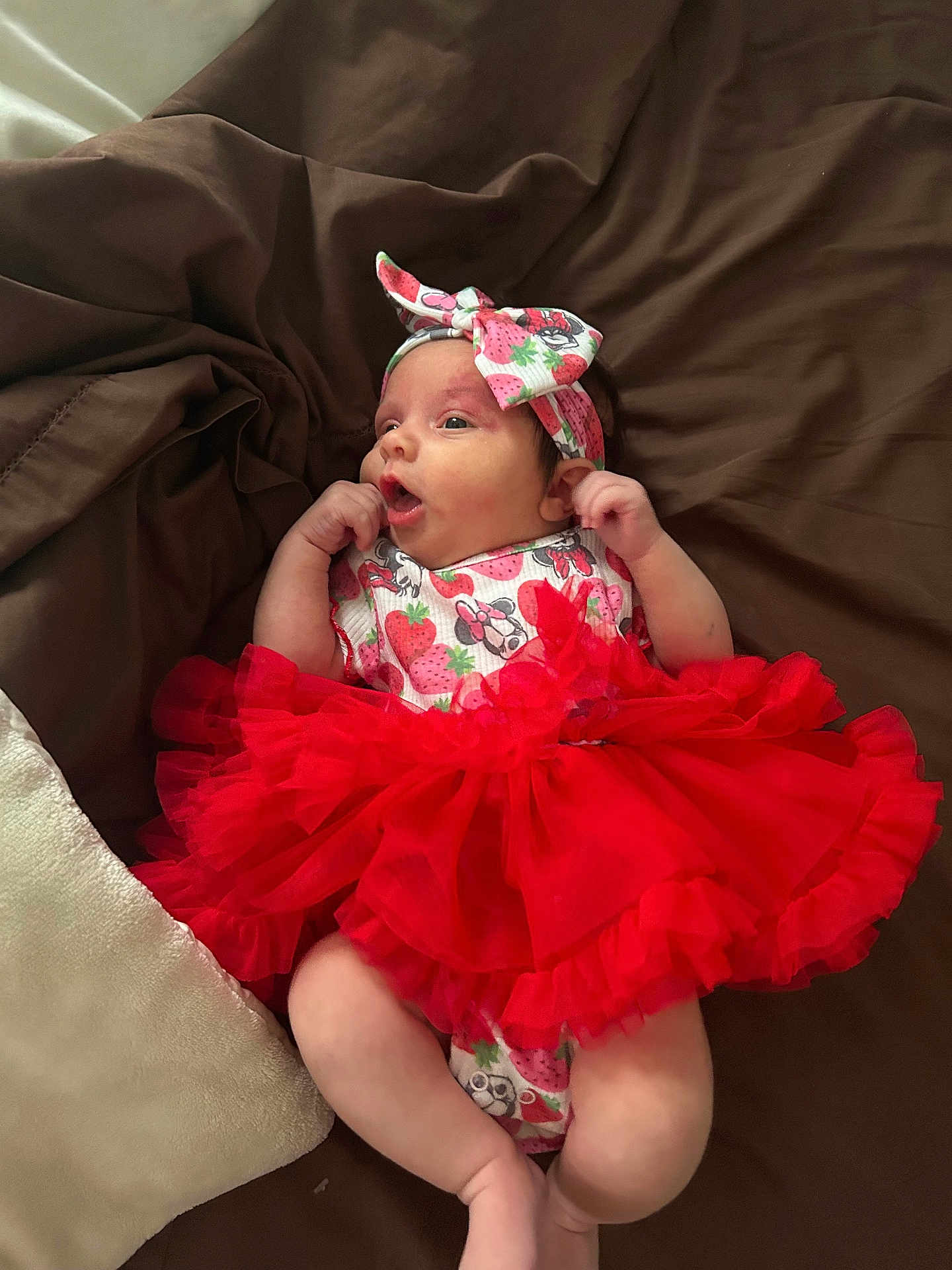 Amara joined the competition — help win amazing prizes! baby, infant, tutu, red, headband, strawberry, blanket, clothing, cute, lying_down, newborn, bed, soft, person, expression, small_hands, fashion, adorable, portrait, colorful