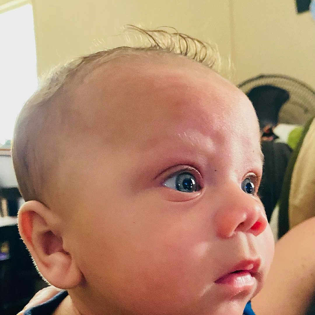 Randy is registered to the contest to win money with this photo: baby, blue_clothing, child, close_up, curious, ear, expression, eyes, face, head, human, indoor, infant, mouth, nose, person, portrait, skin, soft_light, young