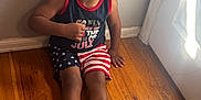 Lyric joined the competition — help win amazing prizes! child, toddler, smiling, curly_hair, sitting, floor, wooden_floor, wall, door, cap, tank_top, shorts, flip_flops, indoors, happy, person, portrait, clothing, american_flag, red_white_blue