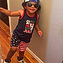 child, boy, indoor, wall, wood_floor, cap, sunglasses, tank_top, shorts, sneakers, smile, curly_hair, patriotic_clothing, red_white_blue, stars, stripes, pose, happy, fashion, casual