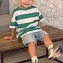 Hugo a rejoint le concours — aidez-le/la à gagner de superbes lots ! child, boy, smiling, green_striped_shirt, denim_shorts, sitting, wooden_table, kicking_feet, living_room, brick_wall, rug, casual_clothing, happy, indoor, furniture, shoes, playful, portrait, person, home