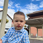 Hugo participe au concours pour gagner de l'argent avec cette photo : toddler, child, boy, blue_shirt, checkered_shirt, outdoor, sky, clouds, table, flowers, playful, face, expression, hair, porch, house, tiles, daylight, casual, cute