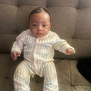 Jayceon is registered to the contest to win money with this photo: baby, infant, child, onesie, couch, furniture, seated, indoors, patterned_clothing, soft_furniture, tufted_couch, cute, calm, young_child, portrait, person, small_hands, small_feet, looking_at_camera, casual