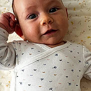 Ellie participe au concours pour gagner de l'argent avec cette photo : baby, infant, face, onesie, clothing, blanket, pattern, floral, smile, hand, lying_down, cute, child, skin, head, eyes, person, indoors, young, portrait
