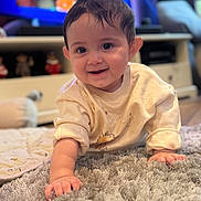 Kaia is registered to the contest to win money with this photo: baby, smiling, crawling, indoor, rug, toy, television, child, face, hand, clothing, home, floor, cute, infant, person, happy, furniture, living_room, cozy