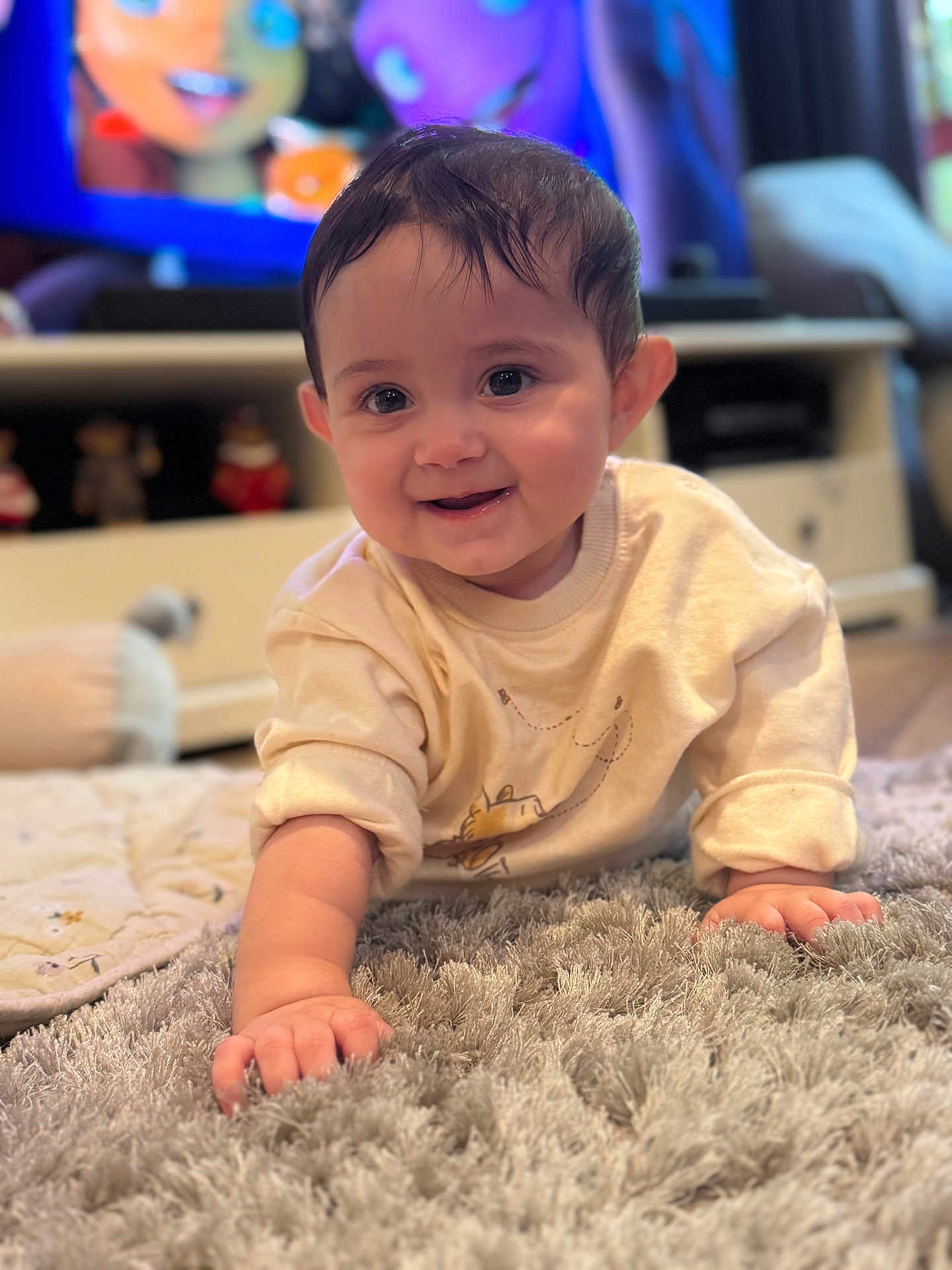 Kaia is registered to the contest to win money with this photo: baby, smiling, crawling, indoor, rug, toy, television, child, face, hand, clothing, home, floor, cute, infant, person, happy, furniture, living_room, cozy