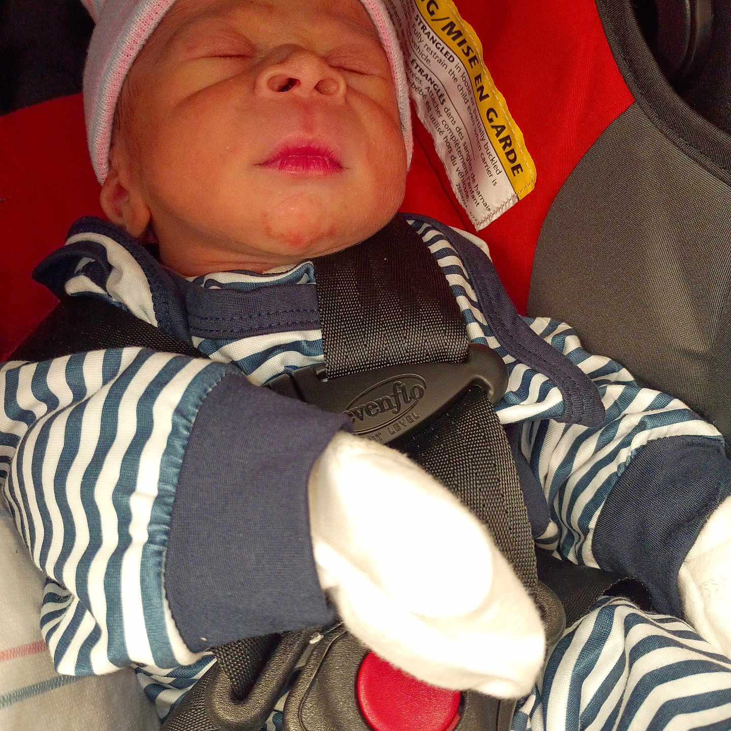 Nehemiah is registered to the contest to win money with this photo: baby, black, blue, car_seat, child, closeup, face, headwear, indoors, infant, mittens, newborn, peaceful, portrait, red, seatbelt, sleeping, striped_clothing, warning_label, white