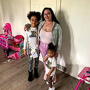 Daniya is registered to the contest to win money with this photo: family, indoor, woman, child, children, door, floor, toy, pink, person, smile, casual, clothing, wood_floor, playroom, glasses, long_hair, standing, crossbody_bag, footwear