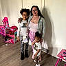 family, indoor, woman, child, children, door, floor, toy, pink, person, smile, casual, clothing, wood_floor, playroom, glasses, long_hair, standing, crossbody_bag, footwear