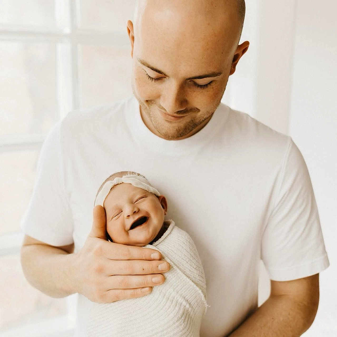 Jacklyn joined the competition — help win amazing prizes! adult, baby, bald, family, father, happy, headband, holding, indoor, love, man, natural_light, newborn, parent, portrait, smile, swaddle, tenderness, white_clothing, window