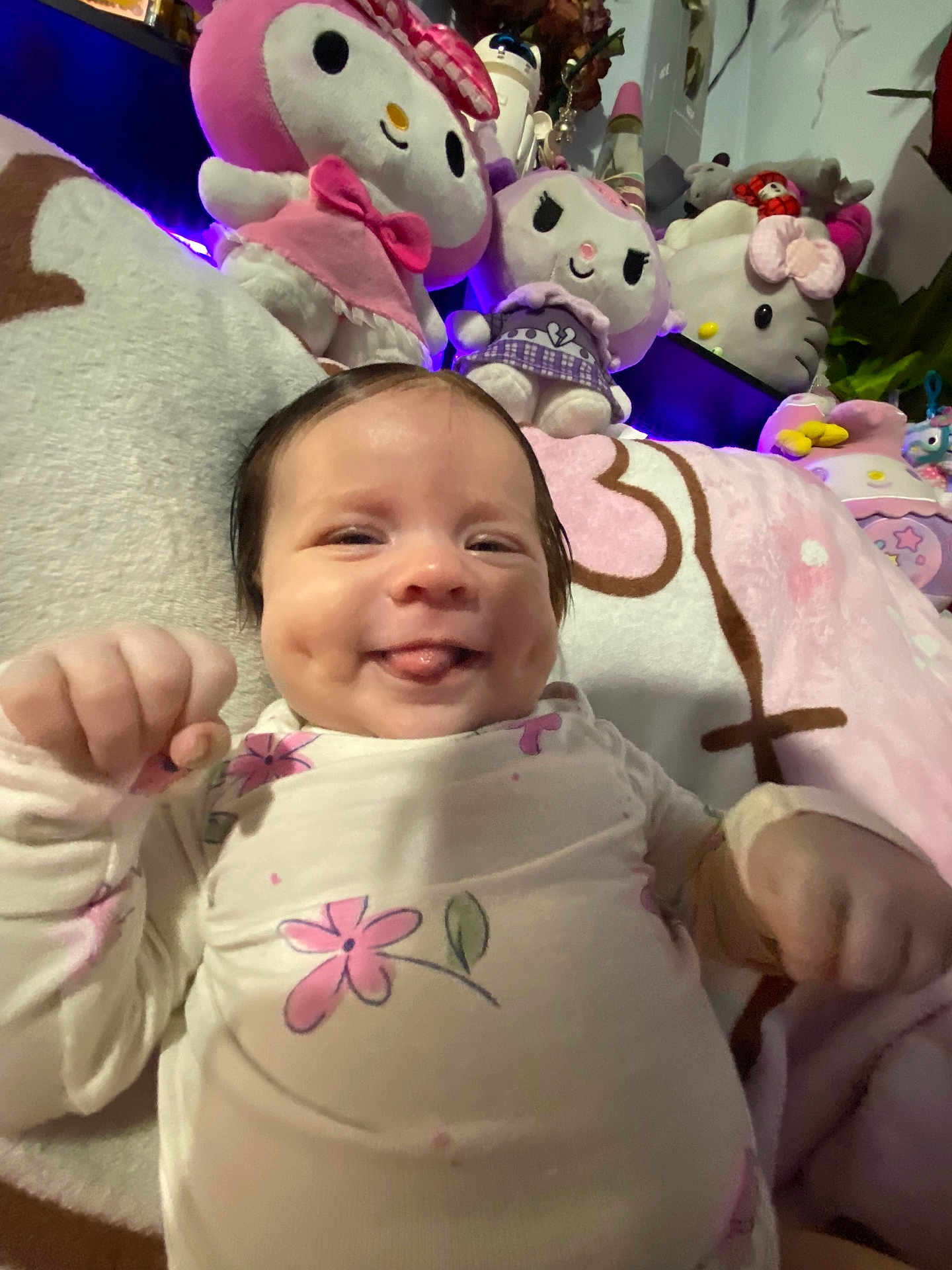 Nova joined the competition — help win amazing prizes! baby, smile, tongue, dimple, plush_toy, blanket, flower_pattern, pink, white_clothing, indoors, cute, child, soft_toy, happy, face, person, cozy, lying_down, home, decor
