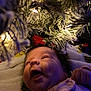 baby, infant, face, smiling, christmas_tree, holiday_lights, blanket, clothing, indoor, closeup, child, winter, festive, joy, cute, cheerful, soft_light, pine_branch, frosted, newborn