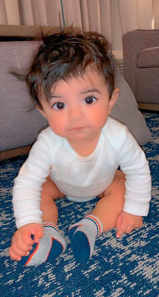 Mark is registered to the contest to win money with this photo: baby, baby_toddler_clothing, cheek, child, comfort, electric_blue, eyelash, finger, flooring, fun, grass, happy, head, human_body, nose, person, sitting, skin, sleeve, t_shirt