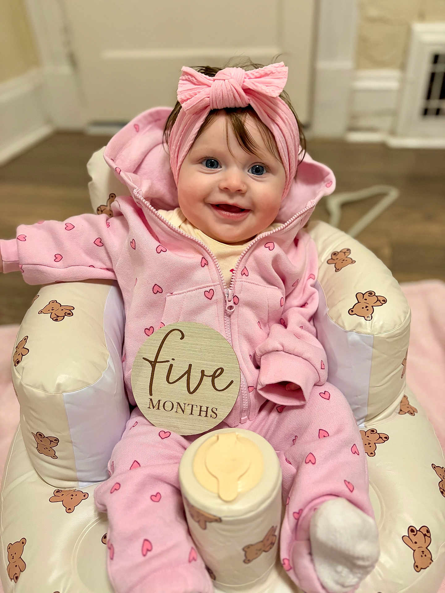 Romi joined the competition — help win amazing prizes! baby, infant, pink_clothing, headband, smiling, sitting, baby_seat, teddy_bear_pattern, indoor, floor, cute, child, portrait, happy, young, cozy, onesie, sock, five_months, wooden_sign