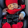 newborn, baby, sleeping, car_seat, red_hat, knitwear, scarf, mittens, booties, blanket, infant, portrait, close_up, indoors, vehicle, harness, seat_belt, peaceful, cozy, vertical_photo