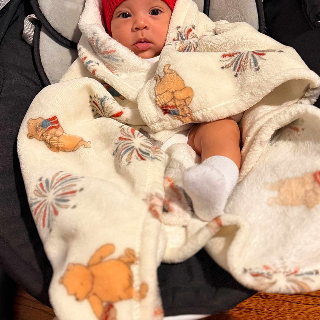 Eithan Gabriel is registered to the contest to win money with this photo: baby, infant, child, red_hat, blanket, teddy_bear, stroller, car_seat, socks, face, wide_eyed, indoors, wooden_floor, portrait, bundled, cozy, seated, baby_clothing, colorful_pattern, photography