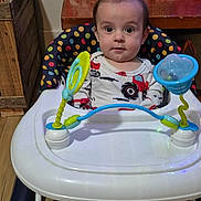 Cooper is registered to the contest to win money with this photo: baby, child, walker, toy, polka_dot, face, indoor, furniture, table, gift_bag, wood_floor, curious, clothing, seat, person, infant, expression, playtime, home, colorful