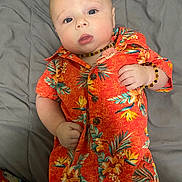 Oliver joined the competition — help win amazing prizes! baby, infant, child, orange_clothing, floral_pattern, bracelet, necklace, lying_down, gray_bedspread, blue_eyes, curious_expression, short_hair, cute, indoors, portrait, closeup, soft_lighting, casual_clothing, skin, person