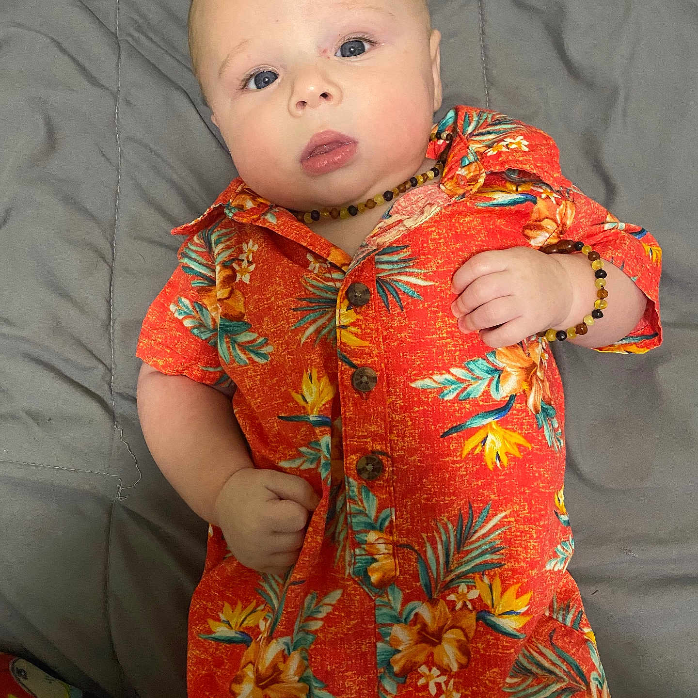 Oliver joined the competition — help win amazing prizes! baby, blue_eyes, bracelet, casual_clothing, child, closeup, curious_expression, cute, floral_pattern, gray_bedspread, indoors, infant, lying_down, necklace, orange_clothing, person, portrait, short_hair, skin, soft_lighting