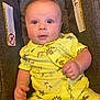 baby, infant, child, yellow_clothing, dinosaur_pattern, car_seat, seat_belt_warning, curious_expression, indoor, portrait, cute, soft_lighting, small_hands, buttoned_shirt, short_sleeves, close_up, person, human, adorable, seated