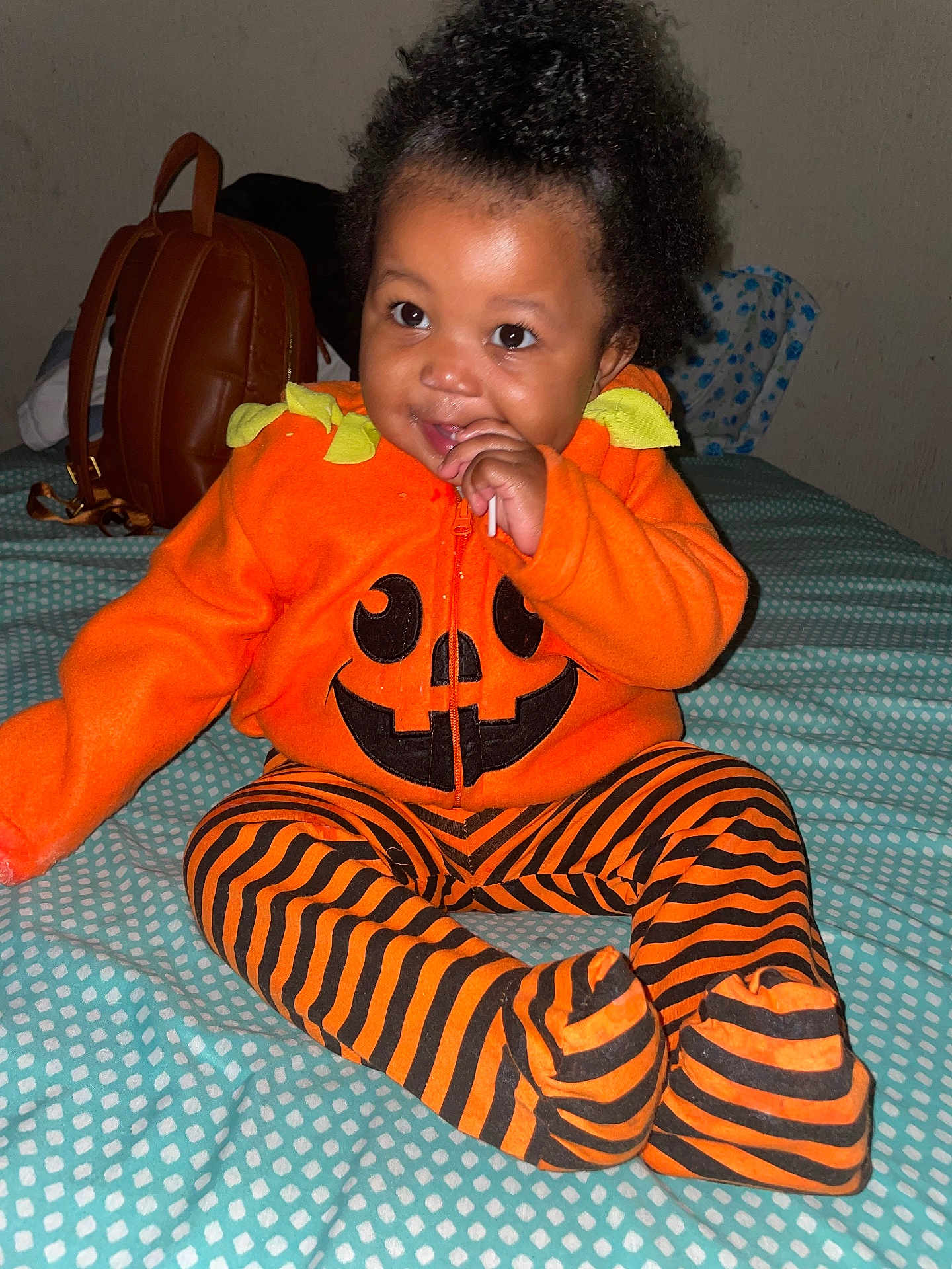 Malaya joined the competition — help win amazing prizes! baby, child, orange, pumpkin, striped_pants, bed, bedspread, lollipop, smile, happy, indoor, black_hair, curly_hair, sitting, clothing, person, cute, infant, backpack, toy